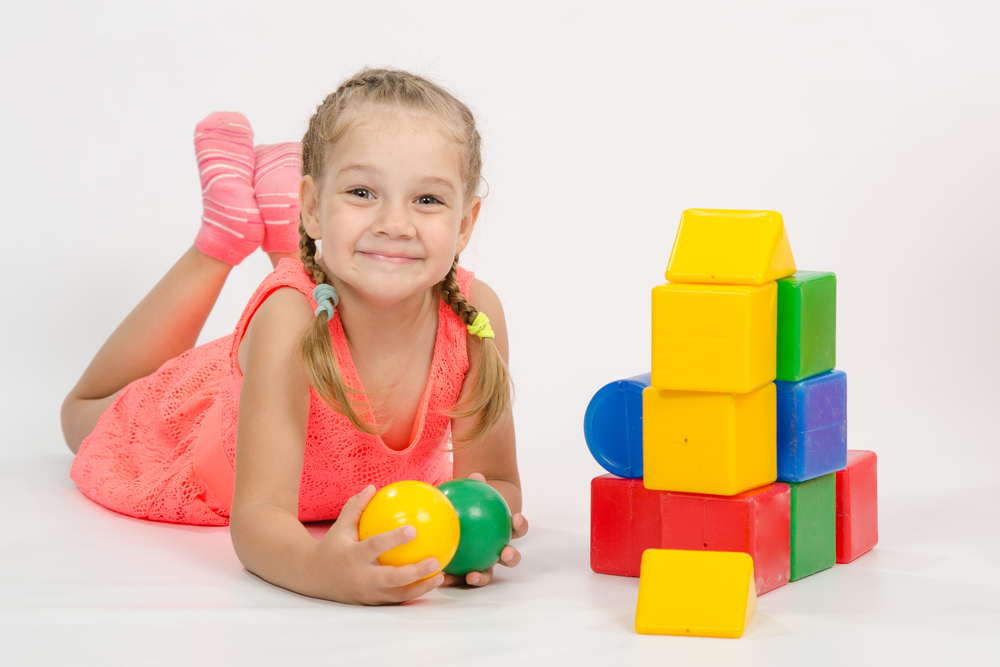 Niña en el suelo jugando con pelotas y bloques de apilar